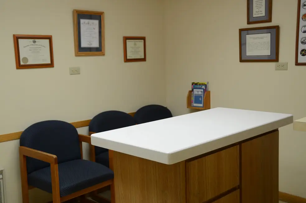 Exam room with framed diplomas above navy chairs and a white-topped oak exam island