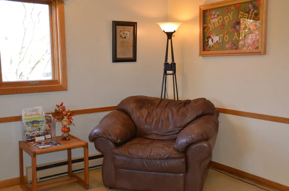 Waiting room corner with a brown leather armchair, a floor lamp and a framed board