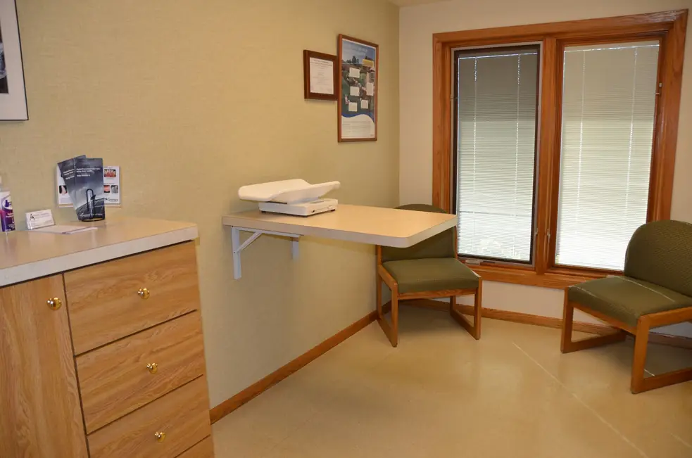 Exam room with a wall-mounted pet scale, oak drawers and green upholstered chairs